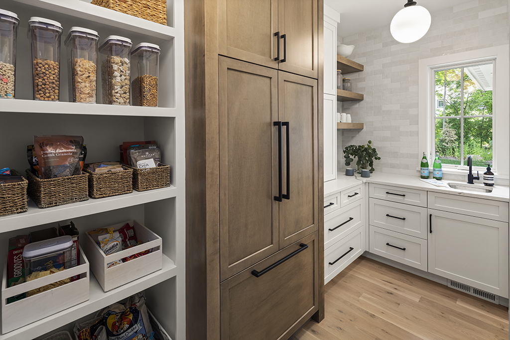 Pantry behind the kitchen with open shelving and refrigerator.