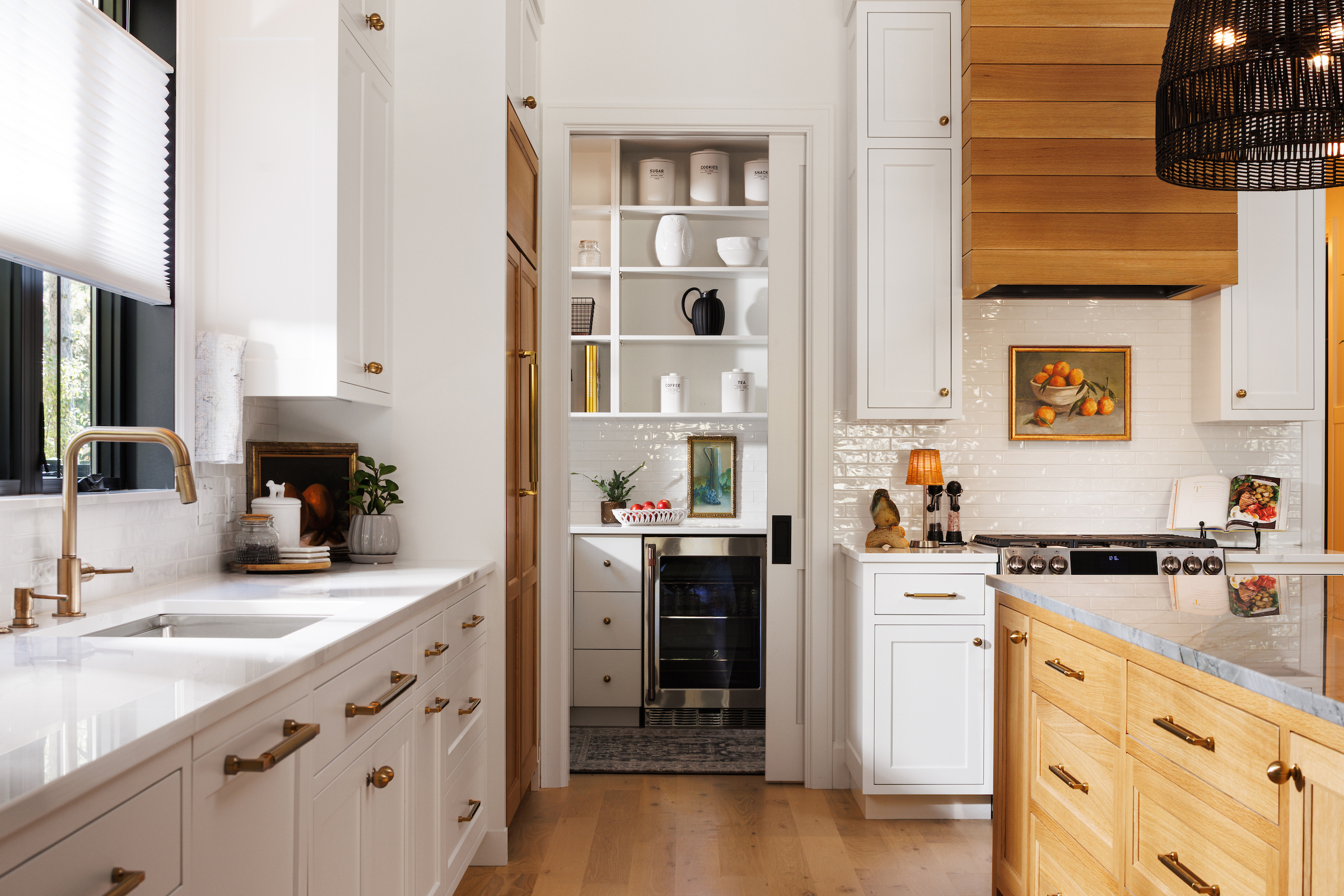 Boyer Building custom new build's kitchen with white cabinetry and accent side pantries for storage - also showing peek a boo to the pantry with sink, mini fridge and other kitchen small appliances.